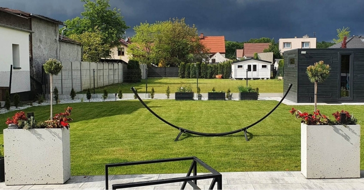 Aranżacja ogrodu z dwiema donicami betonowymi P70 ustawionymi symetrycznie na tle trawnika.