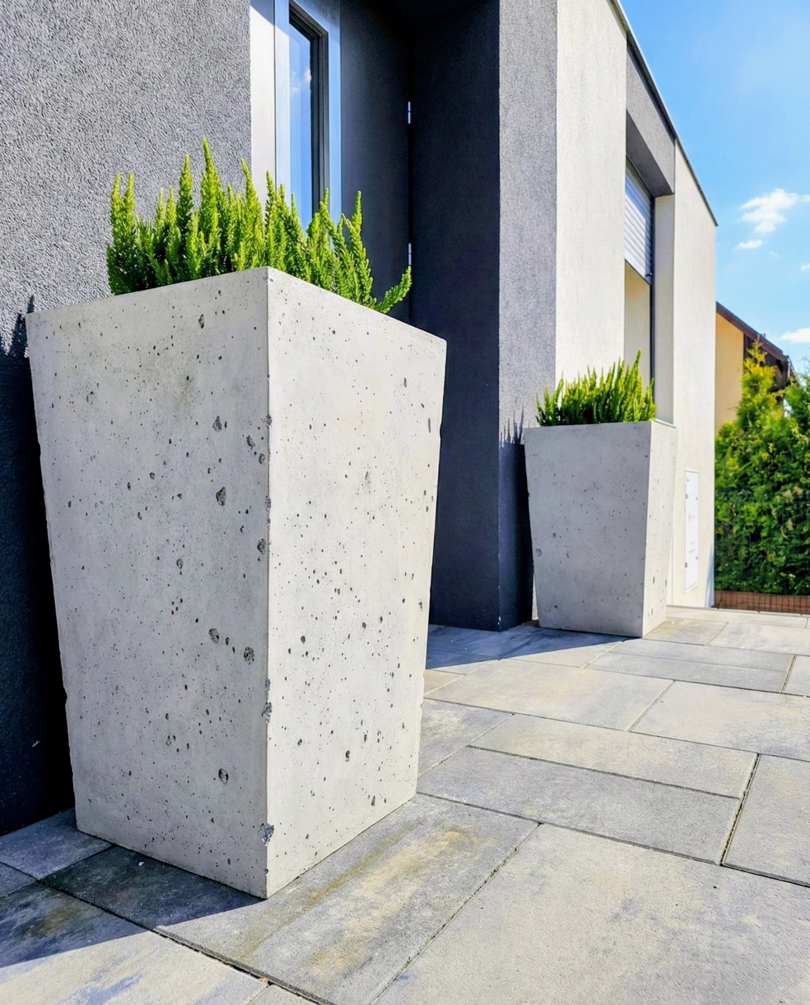 Wysoka donica betonowa Torre 60 37x37x60 cm przed wejściem do budynku